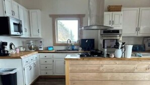 A modern kitchen with white cabinets, a wooden island, and a large window providing natural light.