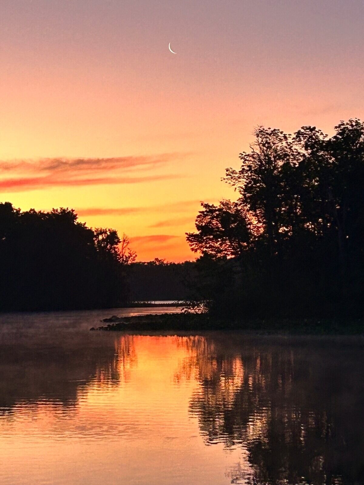 Une étendue d'eau calme qui reflète le ciel au coucher du soleil, entourée d'arbres.