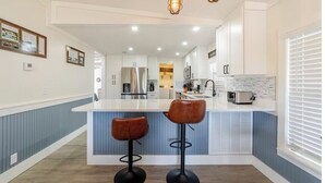 Una cocina moderna con una isla central, taburetes de bar y una araña.