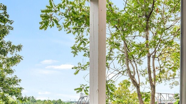 Una terraza de madera con un banco, con vista a un río bordeado de árboles y un puente a lo lejos.