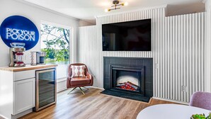 Una sala de estar moderna con chimenea, un televisor montado encima y una zona de cocina con cafetera y licuadora.