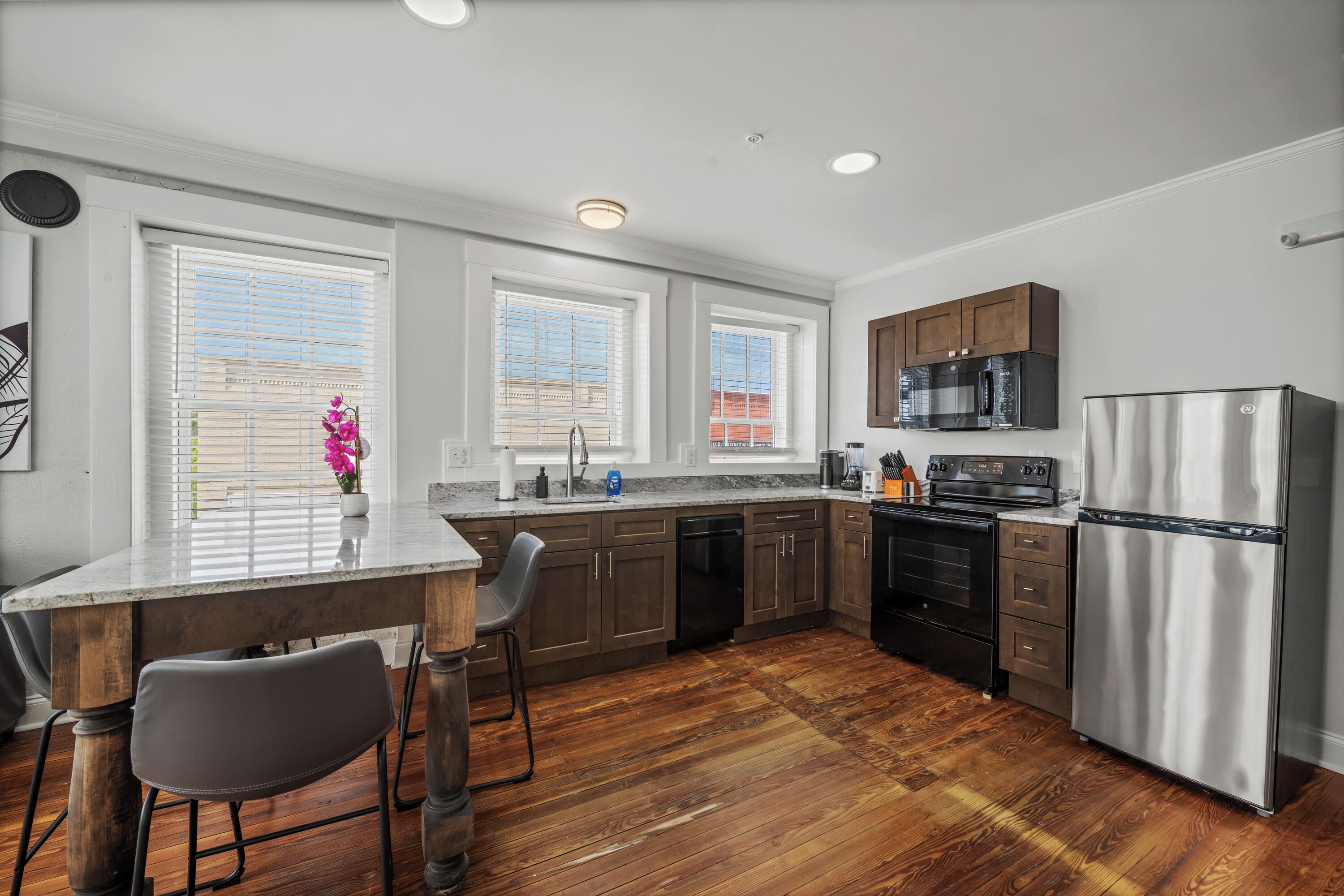A modern kitchen with wooden flooring, built-in appliances, and large windows.