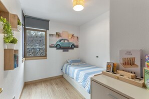Une chambre avec un lit, une fenêtre donnant sur un mur en pierre, un petit bureau avec un jeu de société et une étagère avec des livres et une plante.