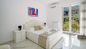 Un dormitorio con cama, mesitas de noche, una ventana con vistas y un cuadro en la pared.