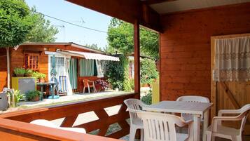 Eine Holzhütte mit einer überdachten Terrasse, ausgestattet mit weißen Plastikstühlen und Tischen.