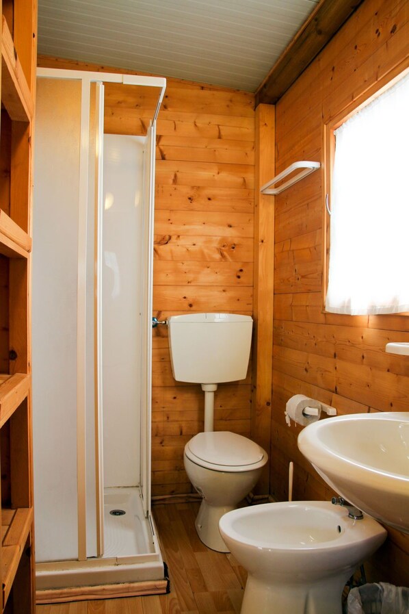 Une salle de bain rustique, aménagée dans une cabane en bois, avec douche, toilettes et lavabo.
