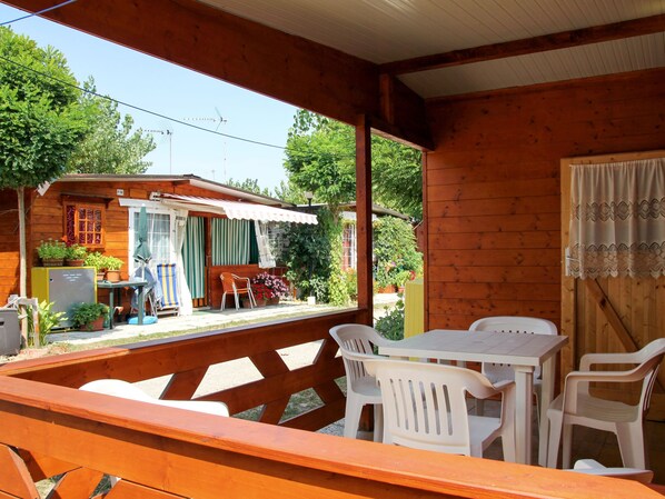A wooden cabin with a covered patio area featuring white plastic chairs and tables.