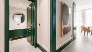 A modern hotel hallway with a green-framed door leading to a bathroom, a large abstract painting on the wall, and a dining area with a table and chairs. - GuestReady - Stylish stay with a balcony (Porto)