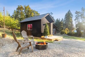 A small cabin with a fire pit and two Adirondack chairs in front. - Lakeside’s Cozy Tiny House Escape - Walk to Beach & Downtown - Pet-Friendly (Lakeside)