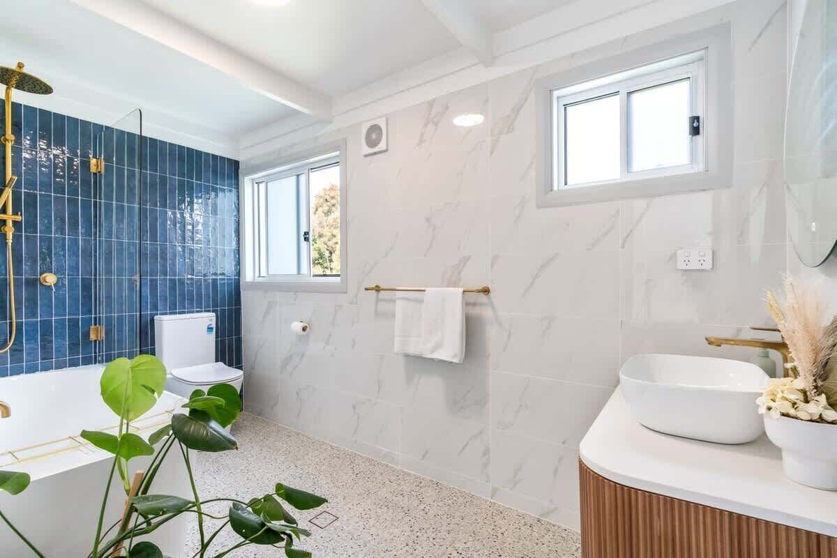Une salle de bain moderne dotée d’une baignoire, de toilettes et d’un lavabo, avec des carreaux bleus, des murs en marbre et une fenêtre.