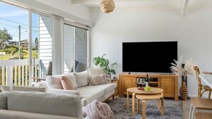 A modern living room with a sofa, TV, and dining area. - Racecourse Beach Coast Shack (Ulladulla)