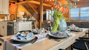 A dining area with a long wooden table set for a meal, a chandelier, and a view of the outdoors. - VIEWS, hot tub, firepit, WIFI and Outdoor Speakers (Bryson City)