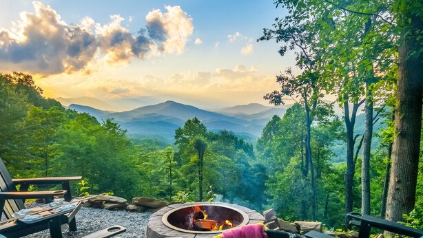 A cozy outdoor seating area with a fire pit, surrounded by lush greenery and mountains in the background. - VIEWS, hot tub, firepit, WIFI and Outdoor Speakers (Bryson City)