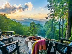 A cozy outdoor seating area with a fire pit, surrounded by lush greenery and mountains in the background. - VIEWS, hot tub, firepit, WIFI and Outdoor Speakers (Bryson City)