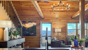 A wooden cabin interior with a kitchen area, a dining table, and a staircase. - VIEWS, hot tub, firepit, WIFI and Outdoor Speakers (Bryson City)