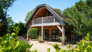 Een houten chalet met balkon, omgeven door groen en een grindpad.