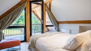 Een slaapkamer met een schuine hemel, een groot raam met gordijnen, een bed en een kleine tafel.