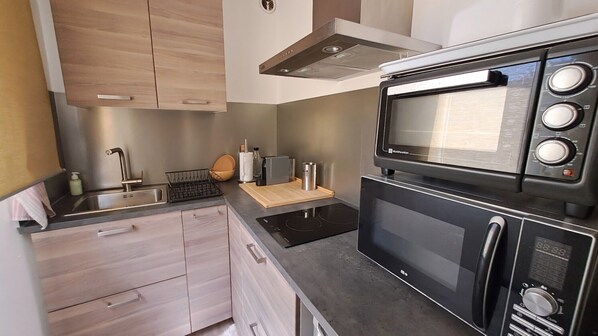Cocina compacta con microondas integrado, horno y placa de cocina, con alacenas de madera clara y diseño moderno.