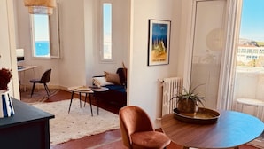 A modern living room with a round wooden table, two chairs, a sofa, and a large window with a view of the sea. - Charming Apartment at 10mn du Vieux Port (Marseille)