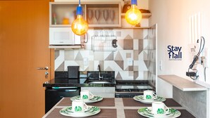 Een moderne keuken met een magnetron, spoelbak en twee hangende lampen. Op een tafel staan twee witte mokken met borden met een bladmotief.