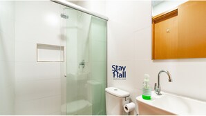 Een moderne badkamer met een glazen douchecabine, een toilet, een wastafel met een zeepdispenser, en een houten kastje boven de wastafel.