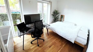 Ein Schlafzimmer mit Bett, Schreibtisch mit Computer und großem Fenster.