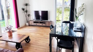 Ein modernes Wohnzimmer mit Flachbildfernseher, einem Esstisch mit Stühlen, einer Couch, einem Couchtisch und einer Topfpflanze.