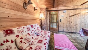 Interior acogedor de una cabaña con pared de madera, un sofá con cojines estampados, una lámpara y una puerta con panel de vidrio.