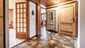 Un pasillo con piso de madera, una puerta de madera con paneles de vidrio y una reja metálica decorativa.