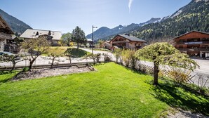 Un pueblo de montaña con edificios de madera tradicionales, una calle pavimentada y una zona arbolada con árboles jóvenes.