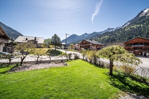 A mountain village with traditional wooden buildings, a paved road, and a grassy area with young trees.