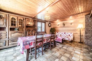 A wooden interior with a dining table, chairs, a sofa, and a chandelier.