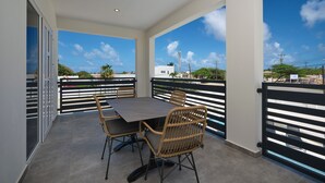 A balcony with a table and chairs, a view of the sky and buildings, and a railing. - Kaikushi (Noord)