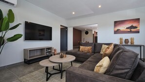 A modern living room with a grey sofa, a round coffee table, and a flat-screen TV mounted on the wall. - Kaikushi (Noord)