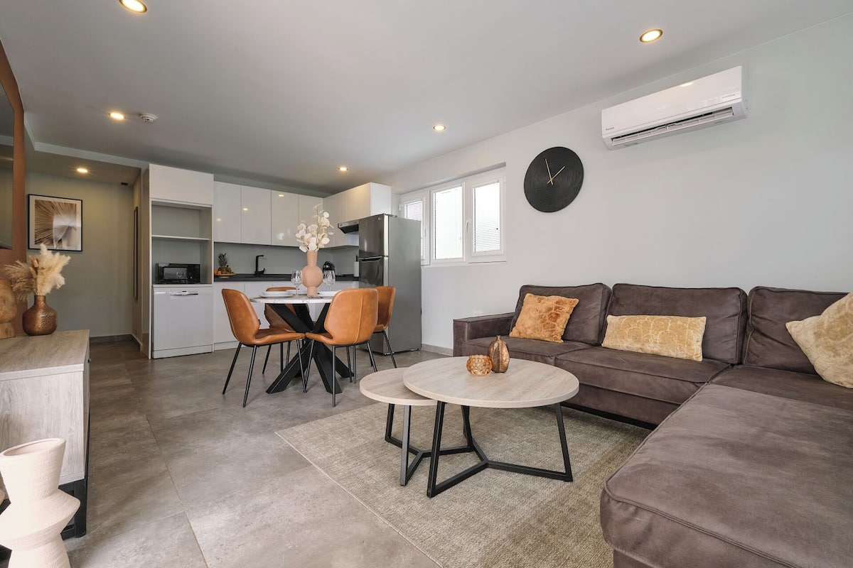 A modern living room with a brown sofa, a round coffee table, and a dining area with a white table and chairs.