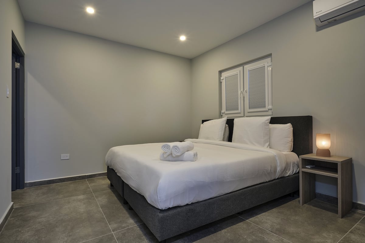 A bedroom with a bed, bedside table, and an air conditioning unit.