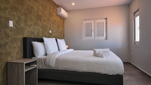 A modern bedroom with a large bed, a bedside table, and a wall-mounted air conditioner. - Kaikushi (Noord)