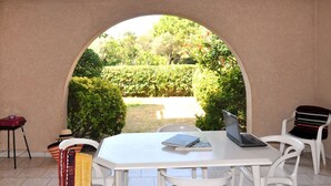 Un porche cubierto con una mesa y sillas blancas, una computadora portátil y un libro.