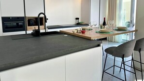 Eine moderne Küche mit einer zentralen Kochinsel, Einbauofen und einem Essbereich mit Tisch für vier Personen.