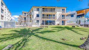 A multi-story residential building with balconies, a well-maintained lawn, and a clear blue sky. - Shoreline Apartments - Unit 15 (Bargara)
