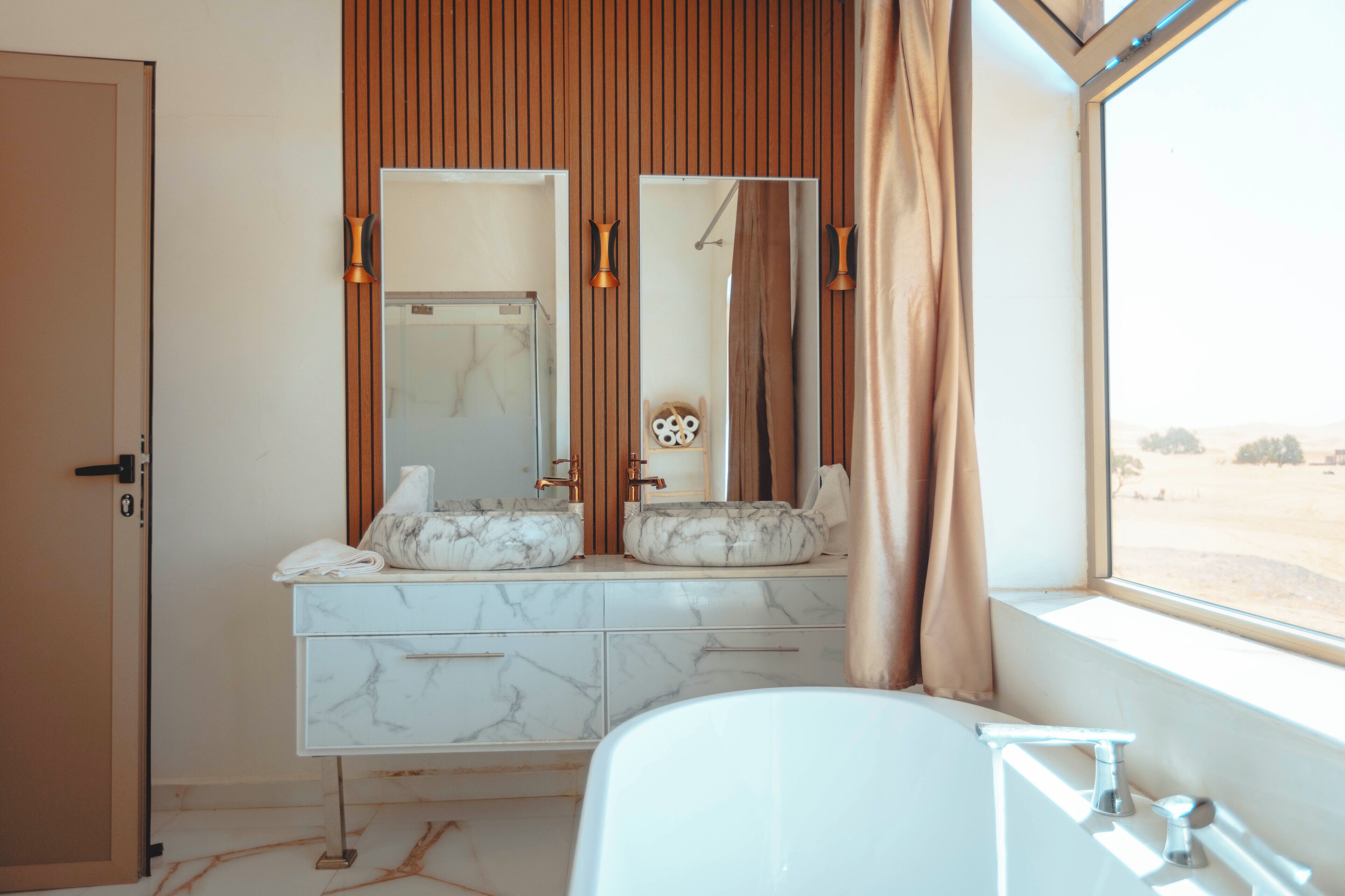 A bathroom with a marble vanity, a large mirror, a bathtub, and a view of a desert landscape through the window.