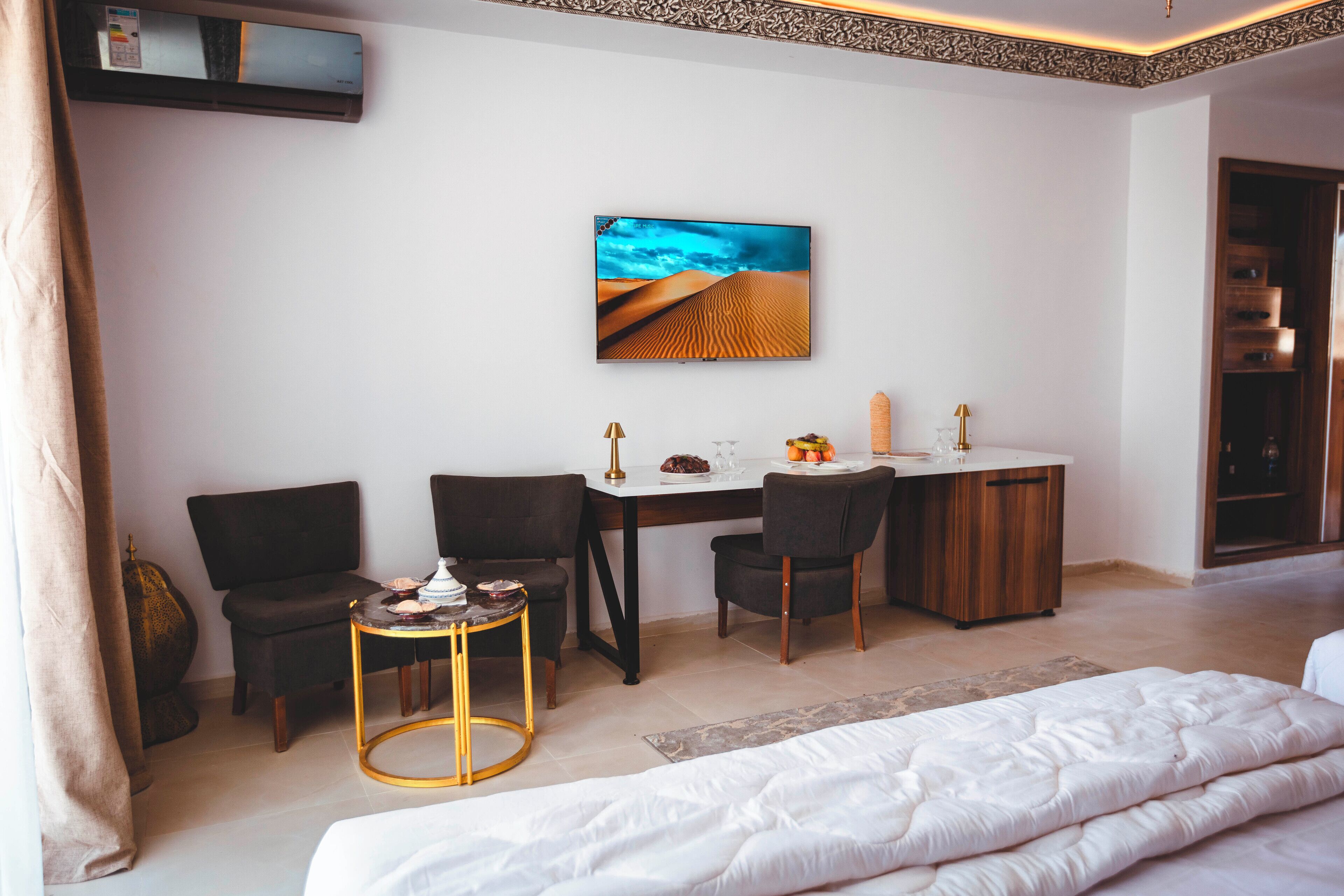 A bedroom with a bed, a desk, two chairs, a small round table, and a wall-mounted TV.