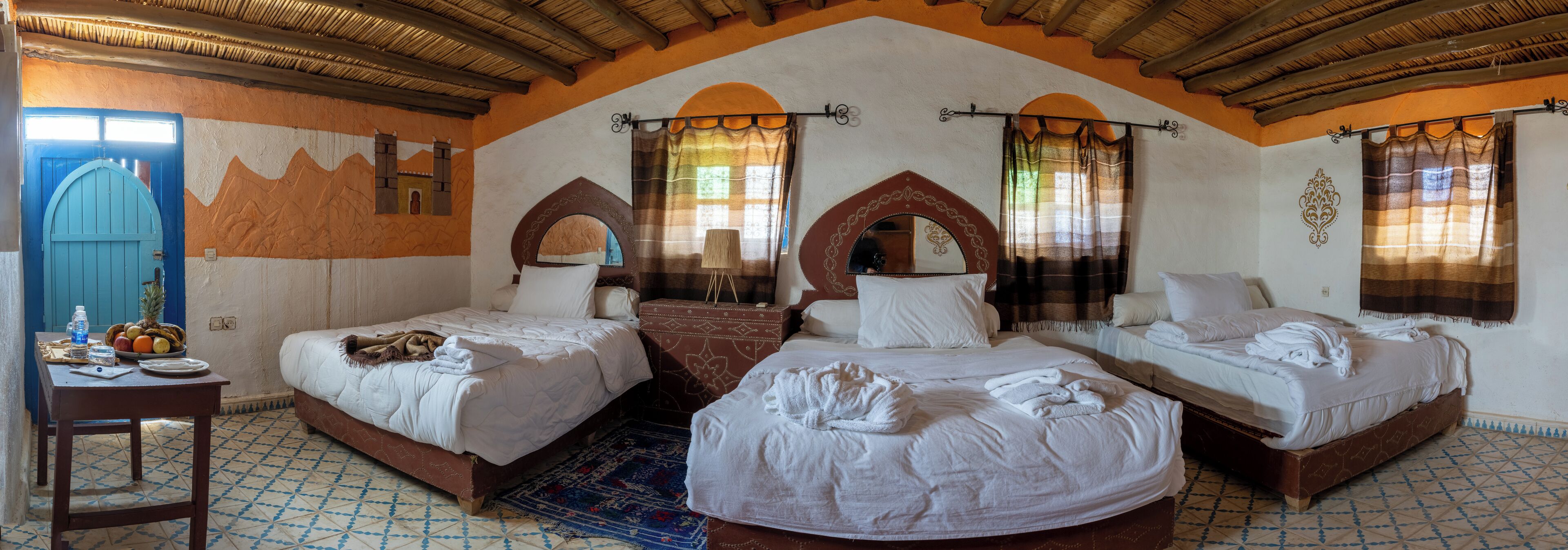 Una habitación con tres camas, una mesa con alimentos para el desayuno y un muro decorativo con motivos de montañas.