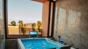 A modern bathroom with a large bathtub, a window with a view of a desert landscape, and marble walls. - Kasbah Merzouga (Taouz)