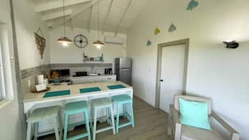A kitchen with a central island, bar stools, a refrigerator, and a dining area with a chair and a table.