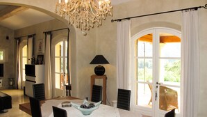 Ein Essbereich mit einer Chandelierleuchtre, einem Tisch mit Spitzenunterlage, Stühlen und einer Schale mit Pralinen.