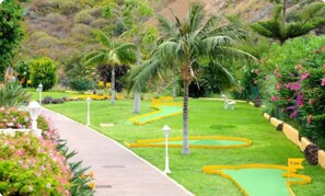 Stroll along the winding garden pathway, bordered by lush greenery and palm trees, to a serene seating area with a bench.