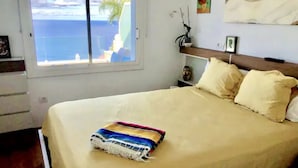 Ein Schlafzimmer mit Bett, einem Fenster mit Meerblick, einem Regal mit Dekoration und einem Gemälde an der Wand.