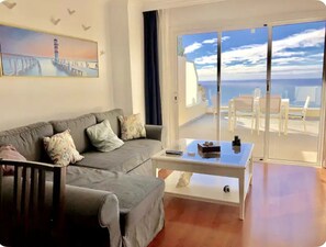 Relax in this stylish living room with a sofa, coffee table, and dining area, leading to a balcony with a sea view.
