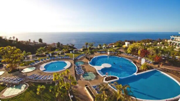 Ein Resort mit mehreren Schwimmbecken, Liegestühlen und Blick auf den Ozean.